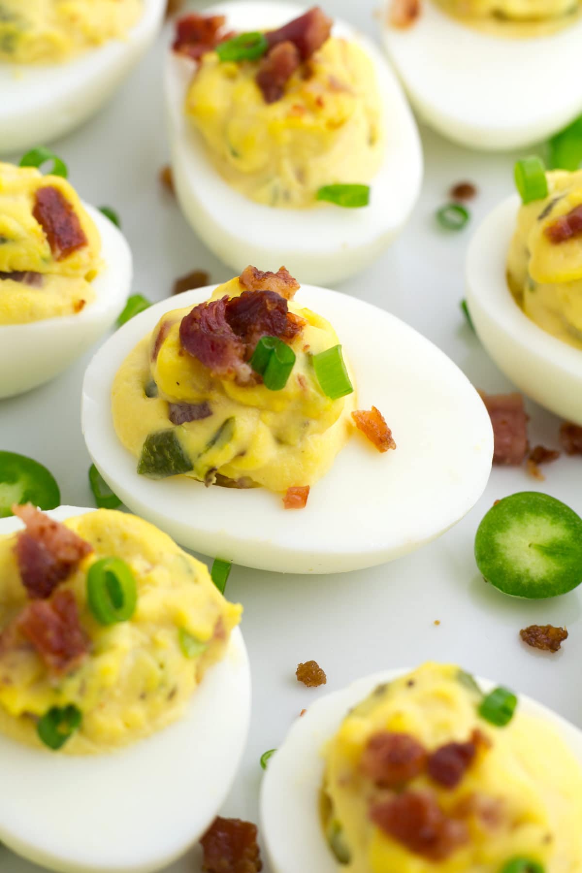 Up close view of egg white filled with deviled egg filling and topped with jalapenos and bacon.