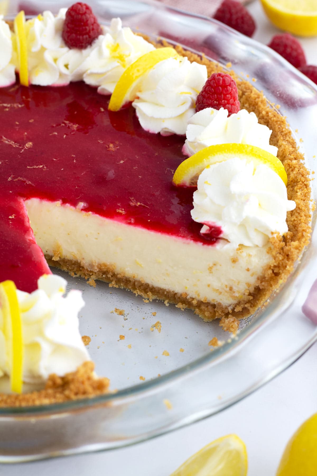 Creamy lemon pie in a clear pie plate with raspberry sauce on top and a slice or pie removed.