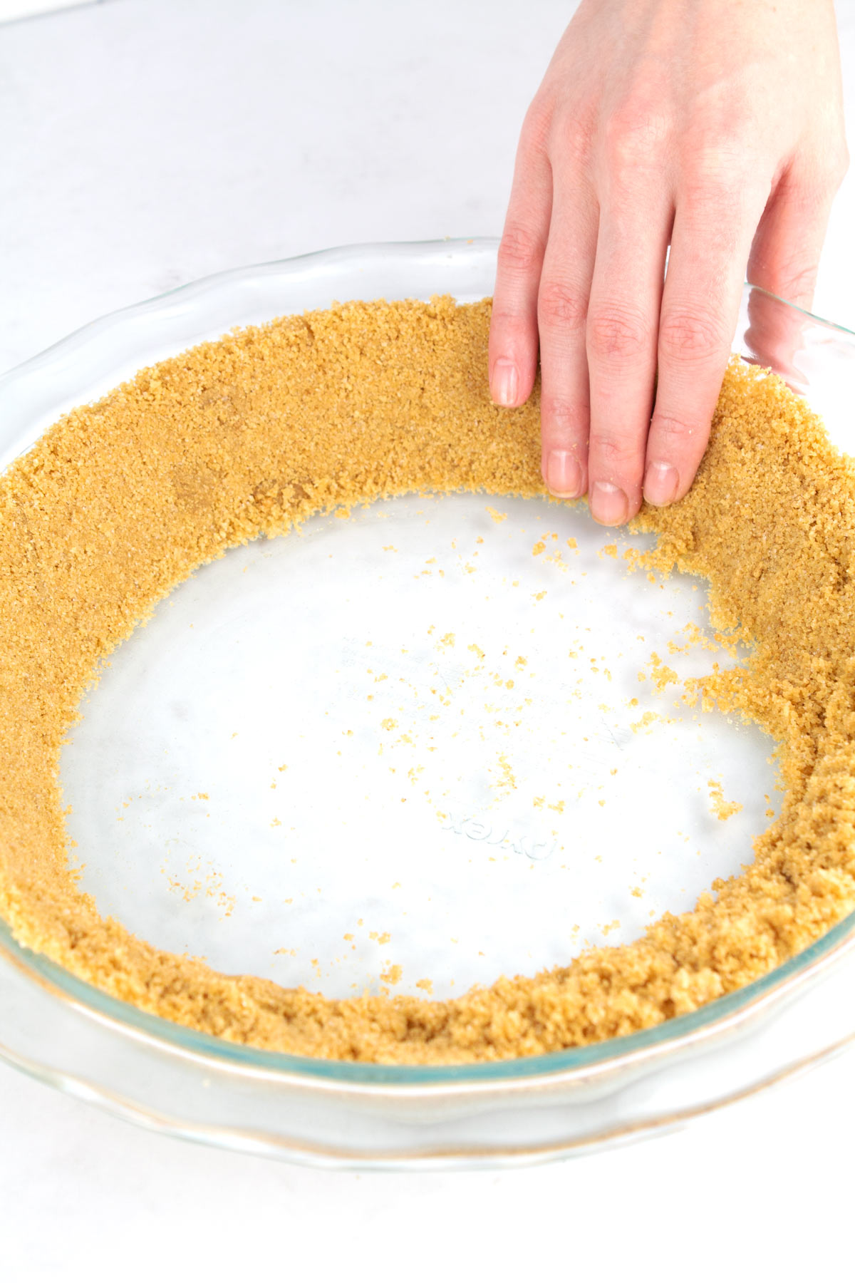 Fingers pressing graham cracker crust into sides of a pie pan.