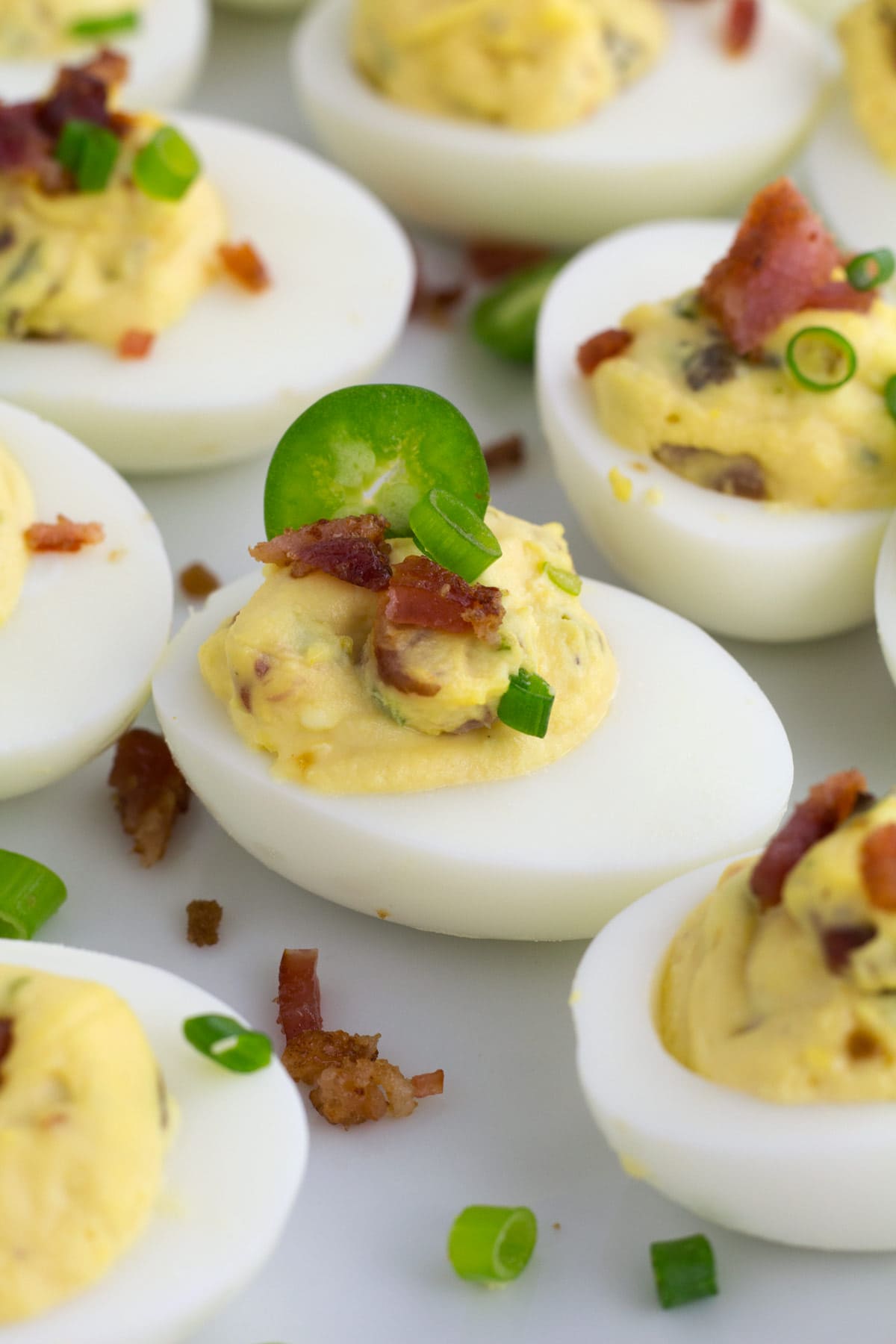 Jalapeno and bacon bits on the top of deviled eggs are on serving platter.