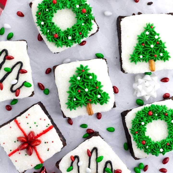 Overhead of assorted Christmas brownies on parchment paper with sprinkles scattered around the scene.