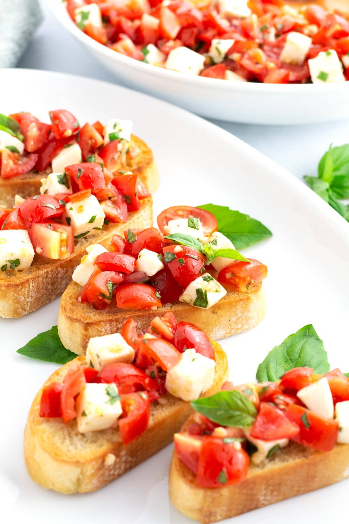 White tray with slices of bruschetta and large serving bowl in the background with extra bruschetta topping.