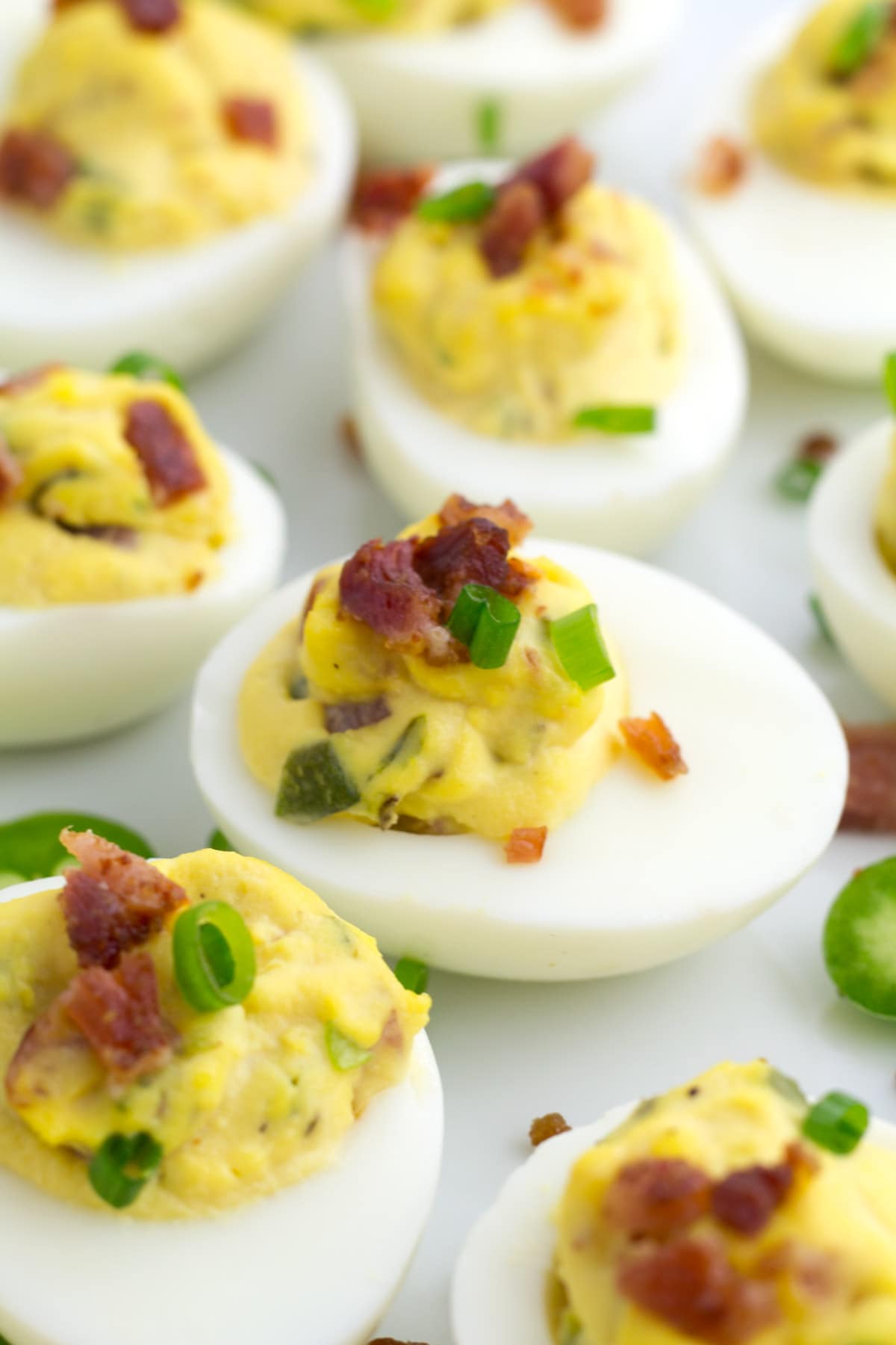 Spicy deviled eggs on platter with bacon and jalapenos.