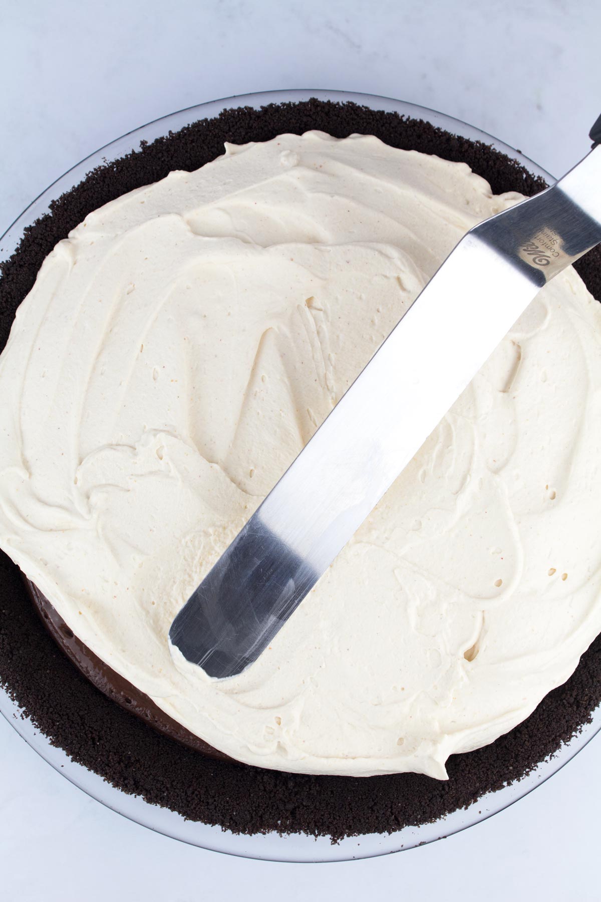 Spatula spreading peanut butter whipped cream over pie filling.