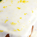 Whole lemon loaf on parchment paper dripping with lemon icing, and with yellow and black text overlay on the picture.