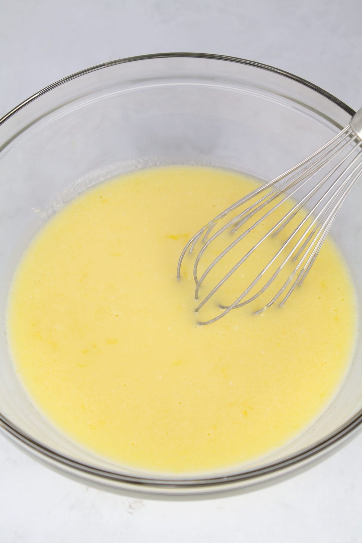 Wet ingredients whisked together in a large glass bowl with the whisk resting in the back of the bowl.