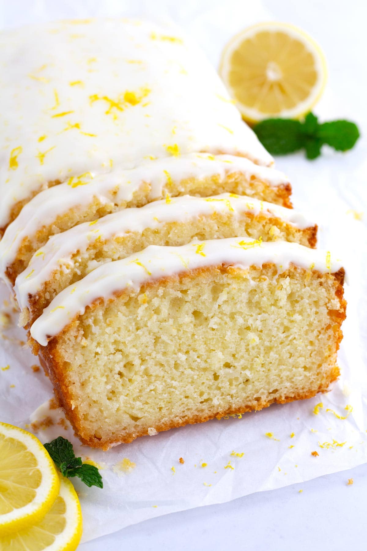 Slices of lemon loaf cake leaning on each other with lemon slices and mint in the background.