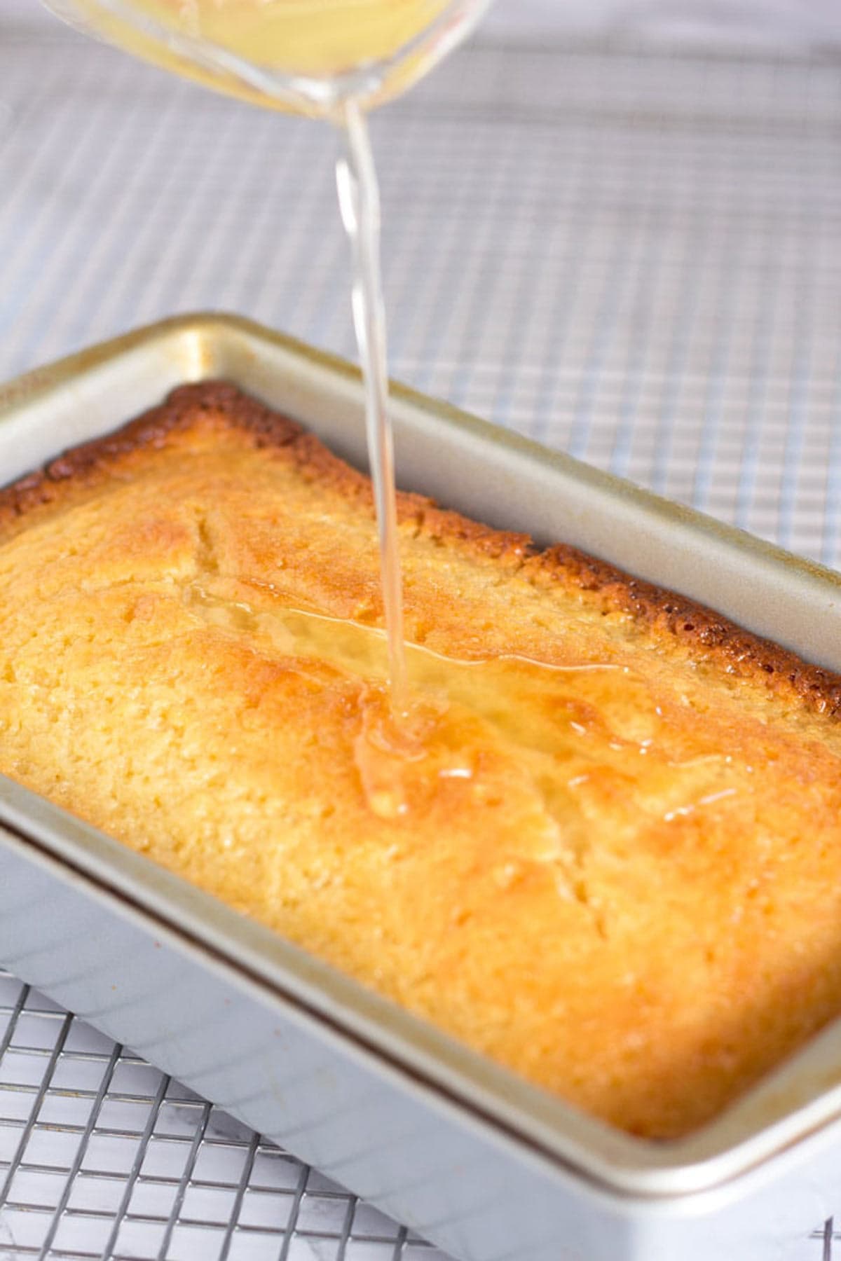 Pouring lemon syrup onto lemon loaf while it is still in the cake pan.