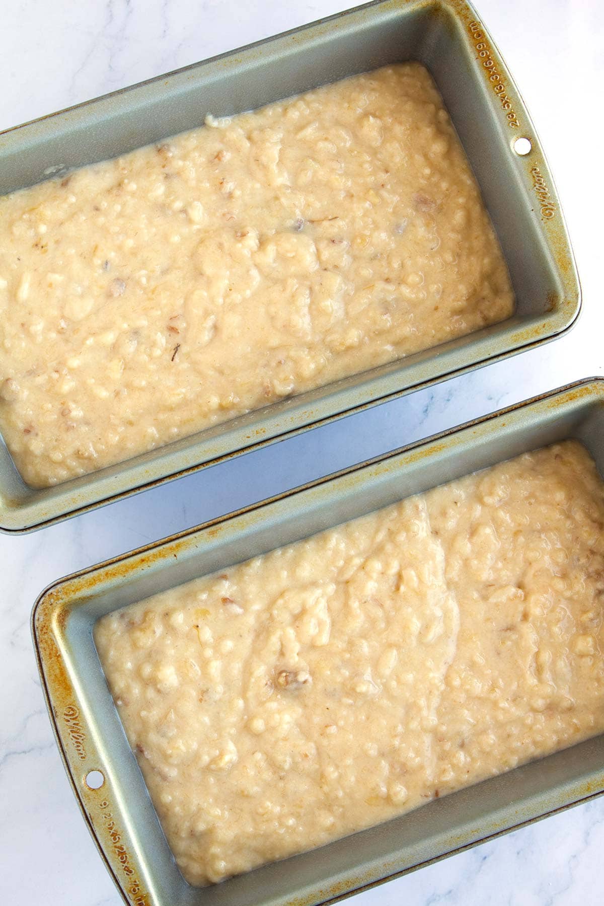Two loaves of banana bread batter in prepared loaf pans.