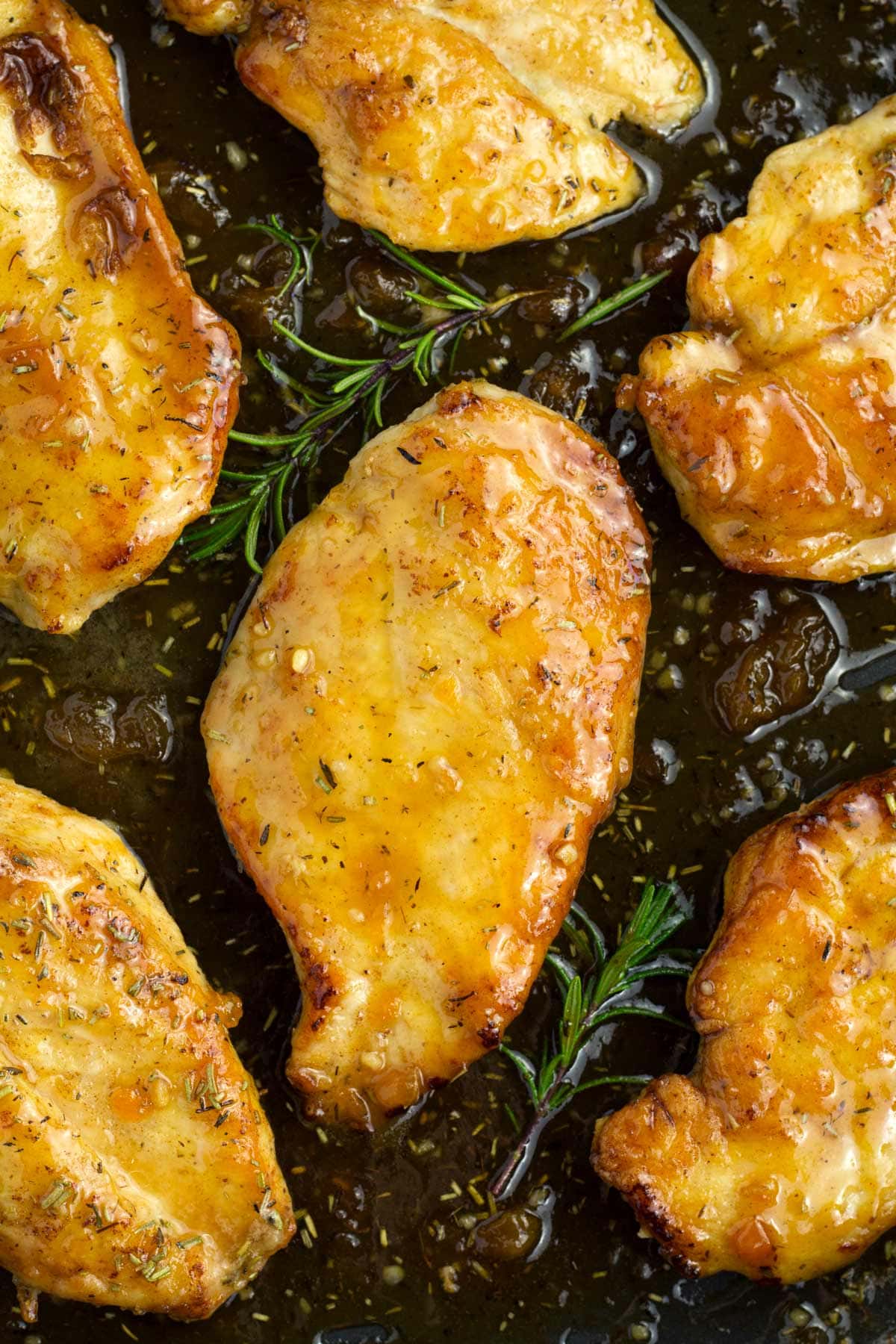 Overhead view of six chicken breasts in a black skillet covered in apricot jam sauce.