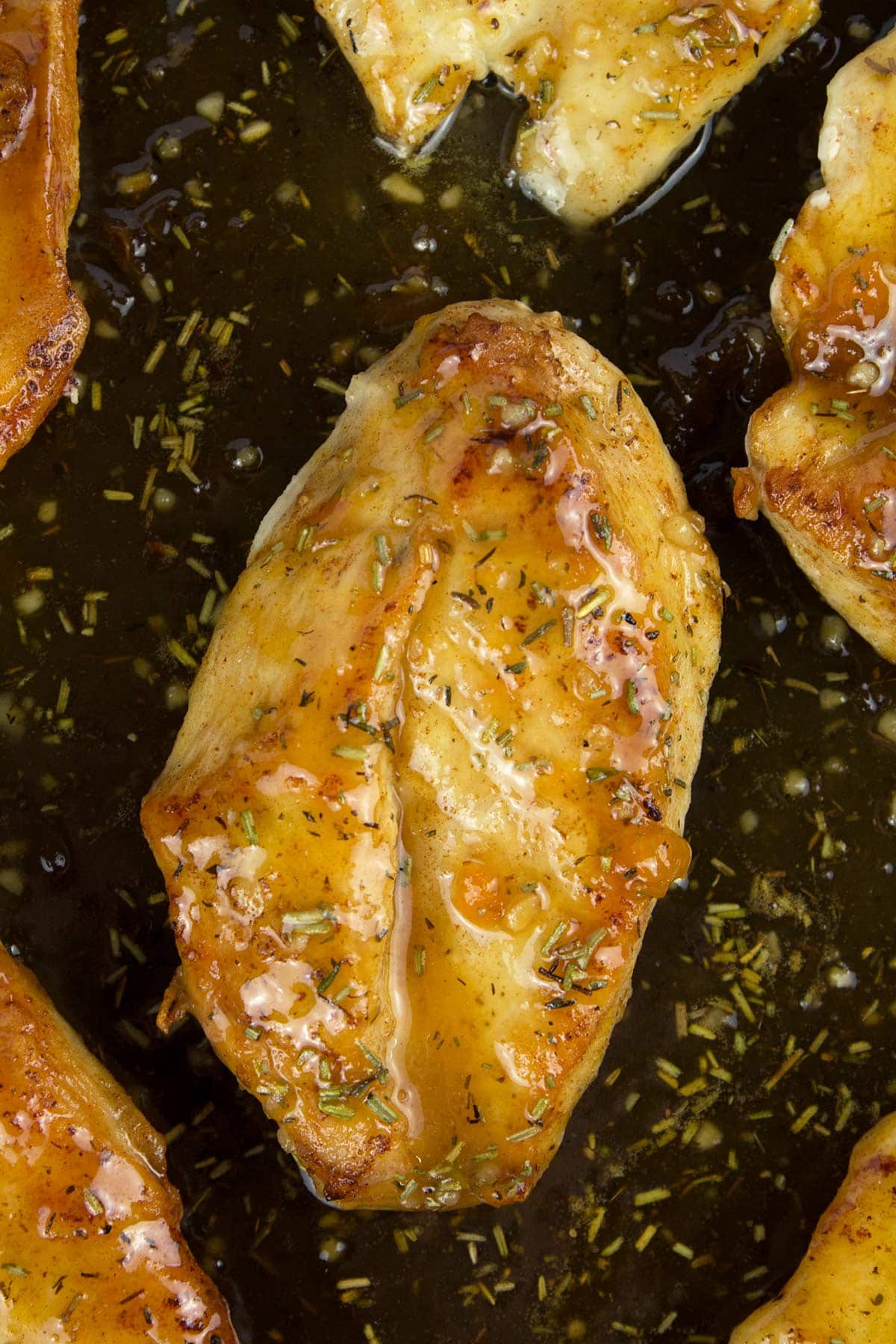 Chicken breasts in a black skillet covered in apricot sauce while they finish cooking.
