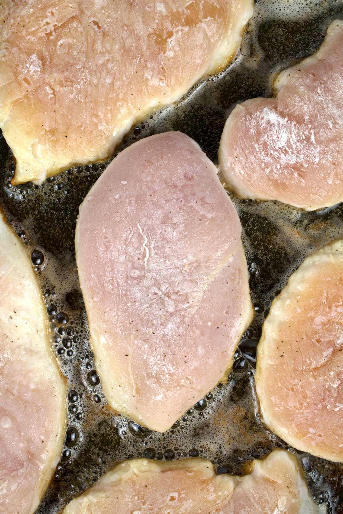 Chicken breasts cooking in melted butter in a black skillet.