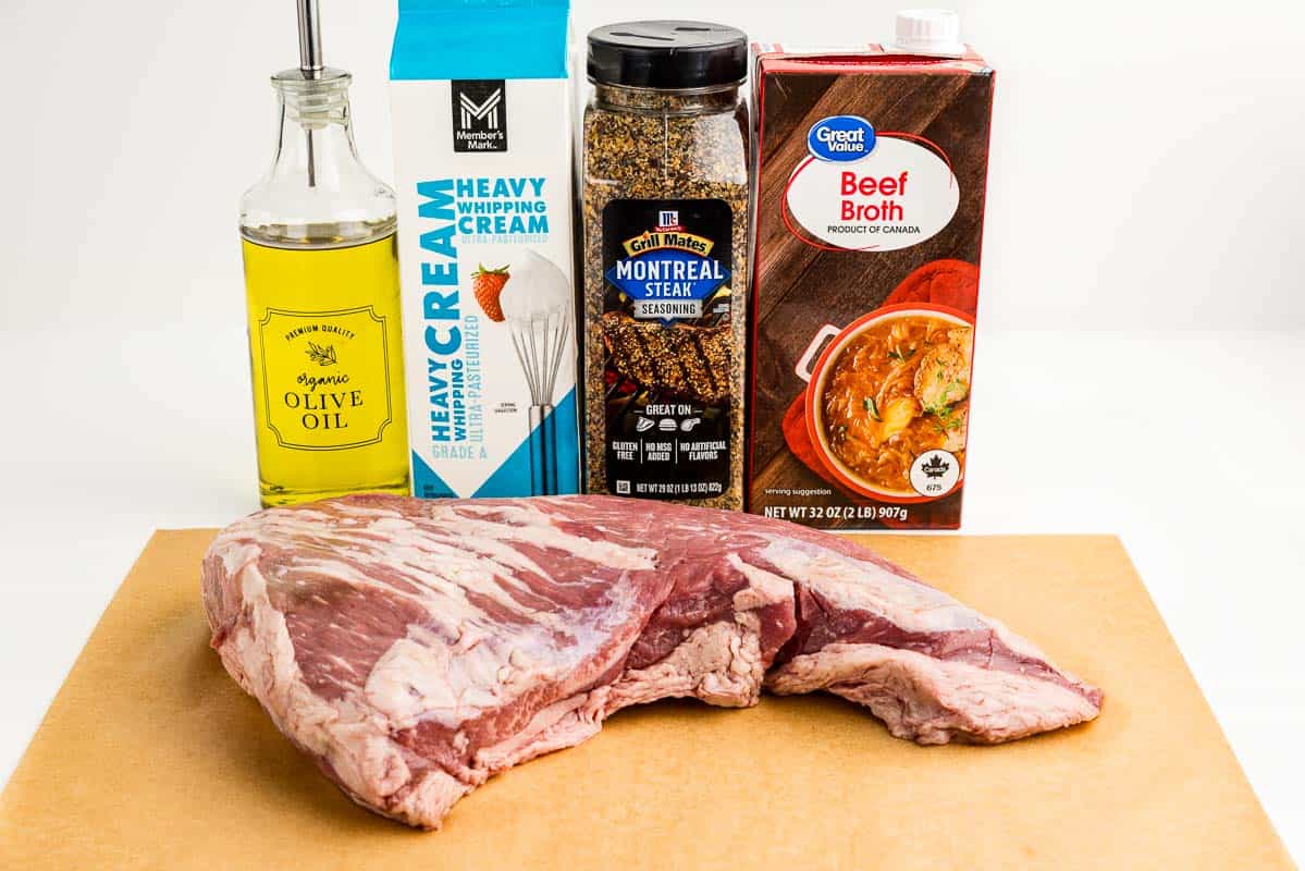 Beef roast, cream, seasoning, oil, and broth on a white cutting board.
