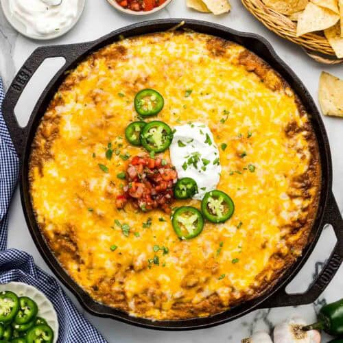 A pan of bean dip with melted cheese and toppings.