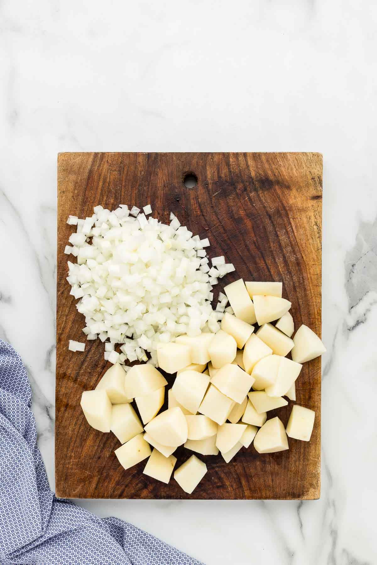 Diced potatoes and onions on a wooden cutting board.