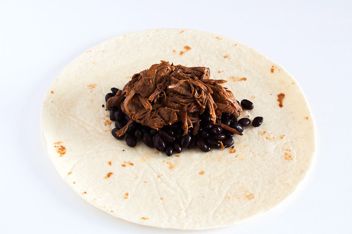 Slow cooker shredded beef on top of black beans in a tortilla.