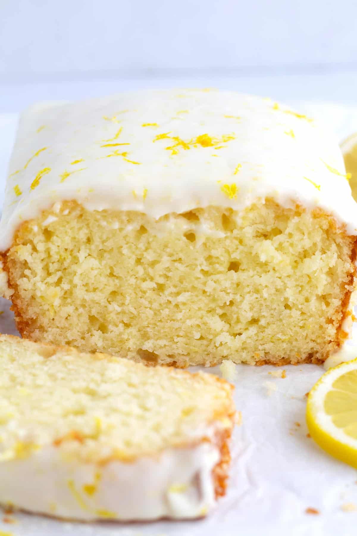 Loaf cake slice open with a thick layer of lemon glaze on top and a slice of cake in the foreground.