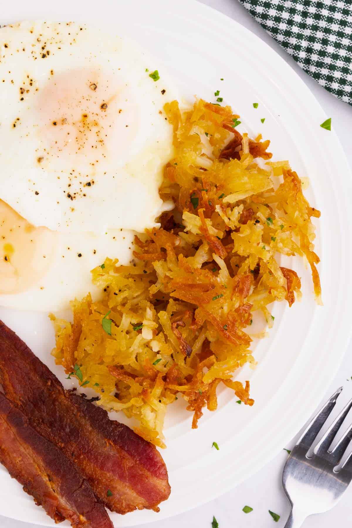 Eggs, bacon, and hash browns on a white plate with a fork beside it.