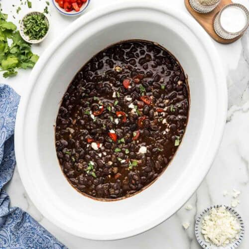 Black beans in the slow cooker with an array of seasonings around it.