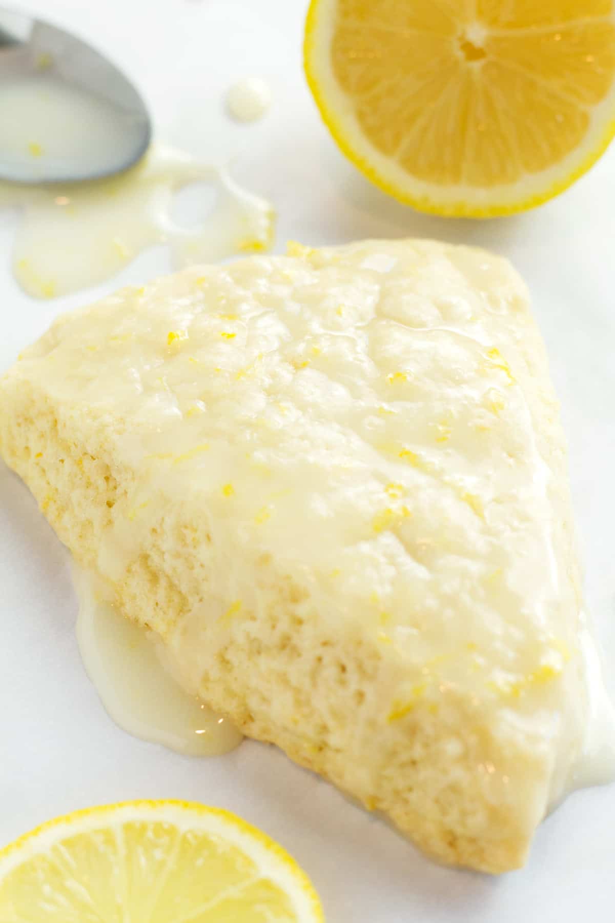 Lemon scone with lemon icing dripping around it and lemon wedges in background.