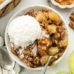 A bowl of apple crisp and ice cream with a spoon on the side.