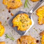 A spatula lifting a smashed potato from a baking sheet.