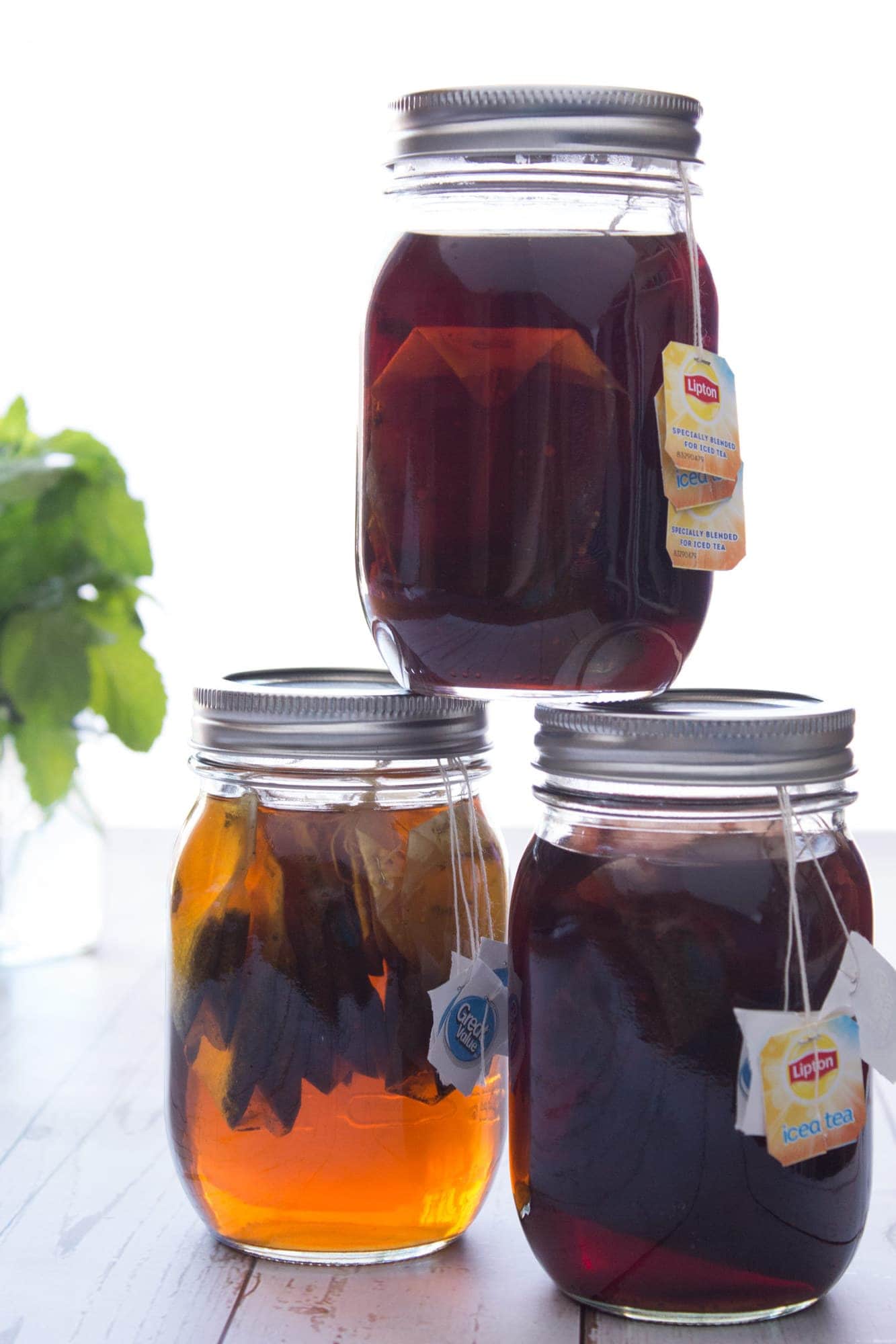 Three jars of tea concentrate stacked off center with herbs in background.