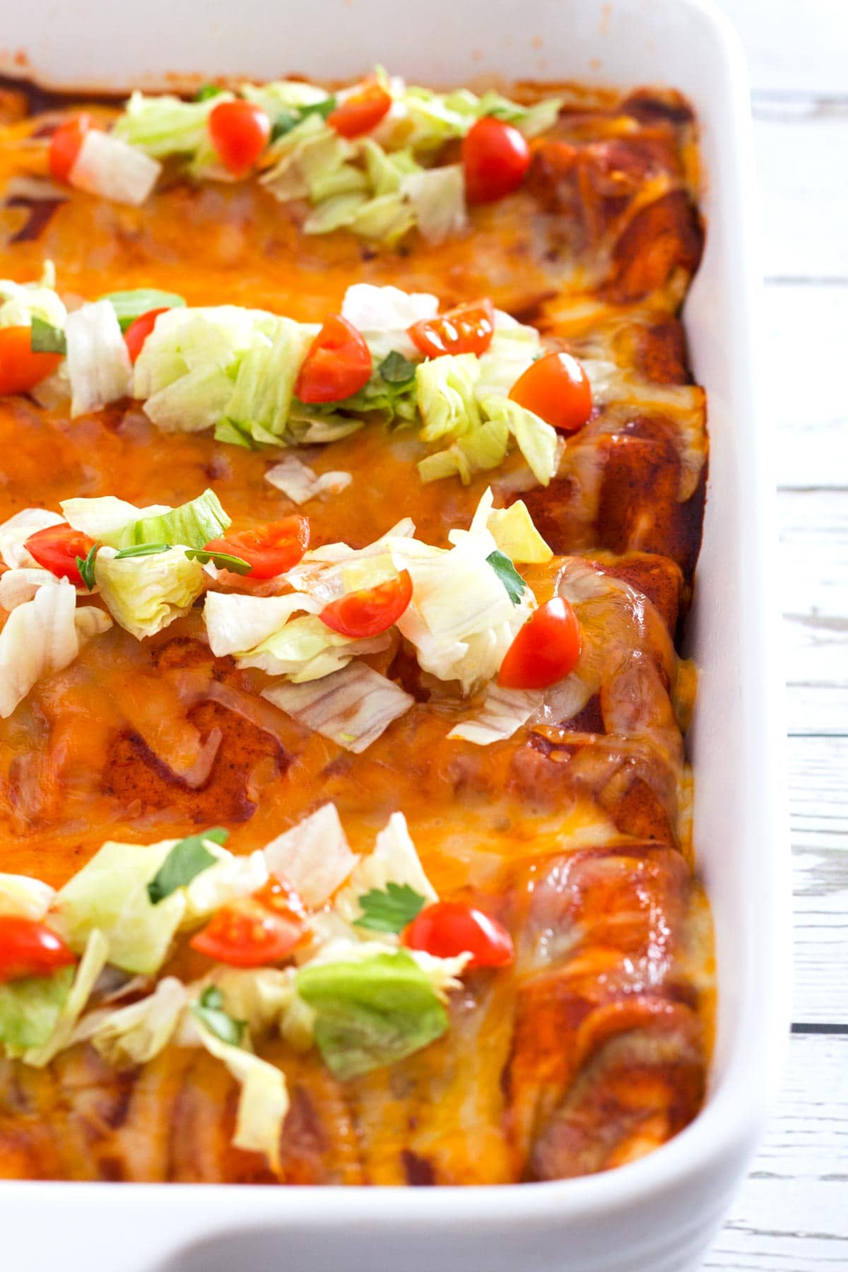 Burritos covered in enchilada sauce, cheese, and topped with lettuce and tomato.