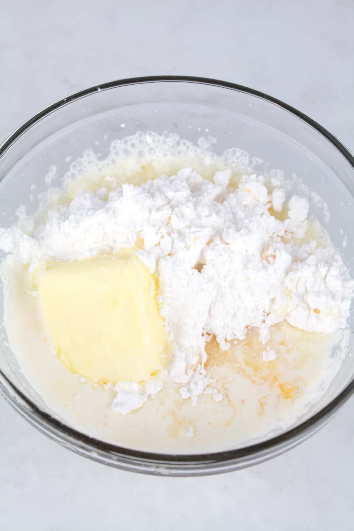 Ingredients for orange icing in a glass bowl.