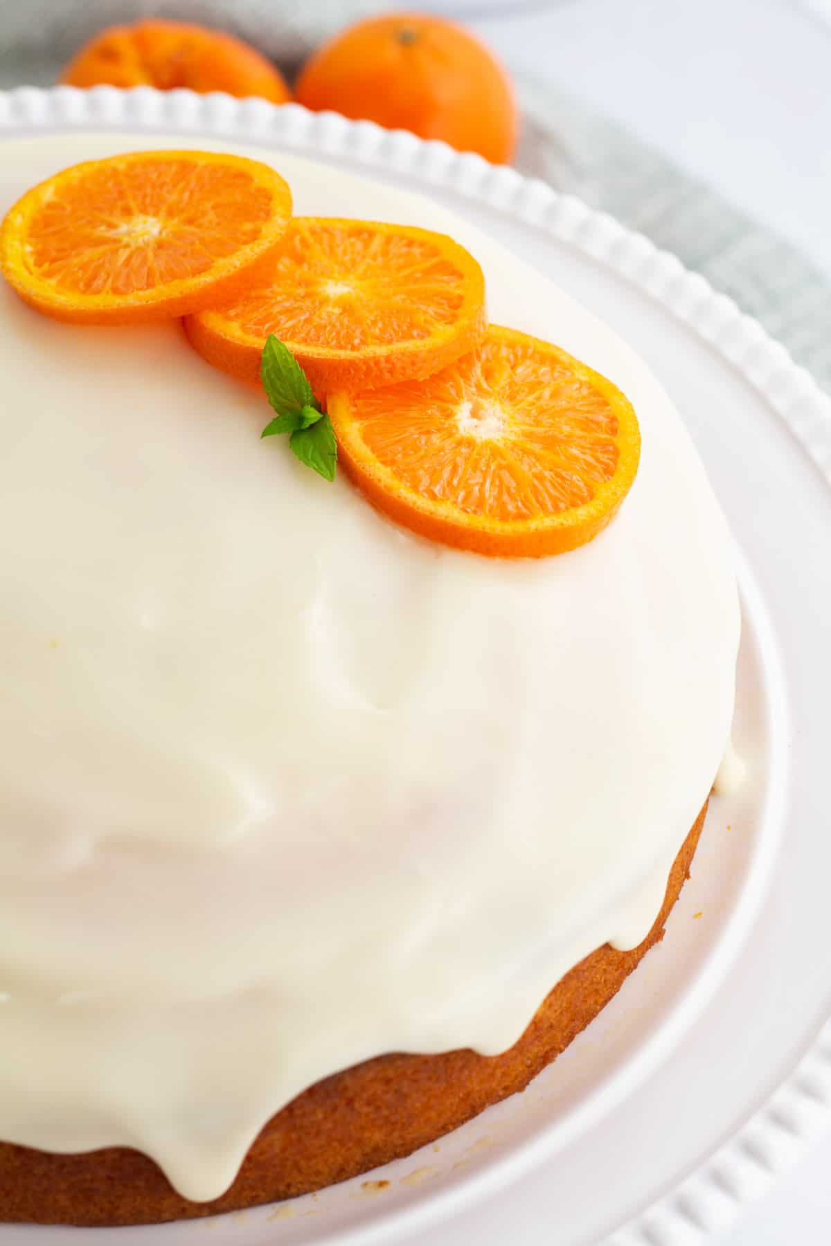Whole clementine cake with white icing and slices of fresh clementines decorating the top.