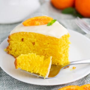 Slice of clementine cake on white plate with a bite removed on a fork.