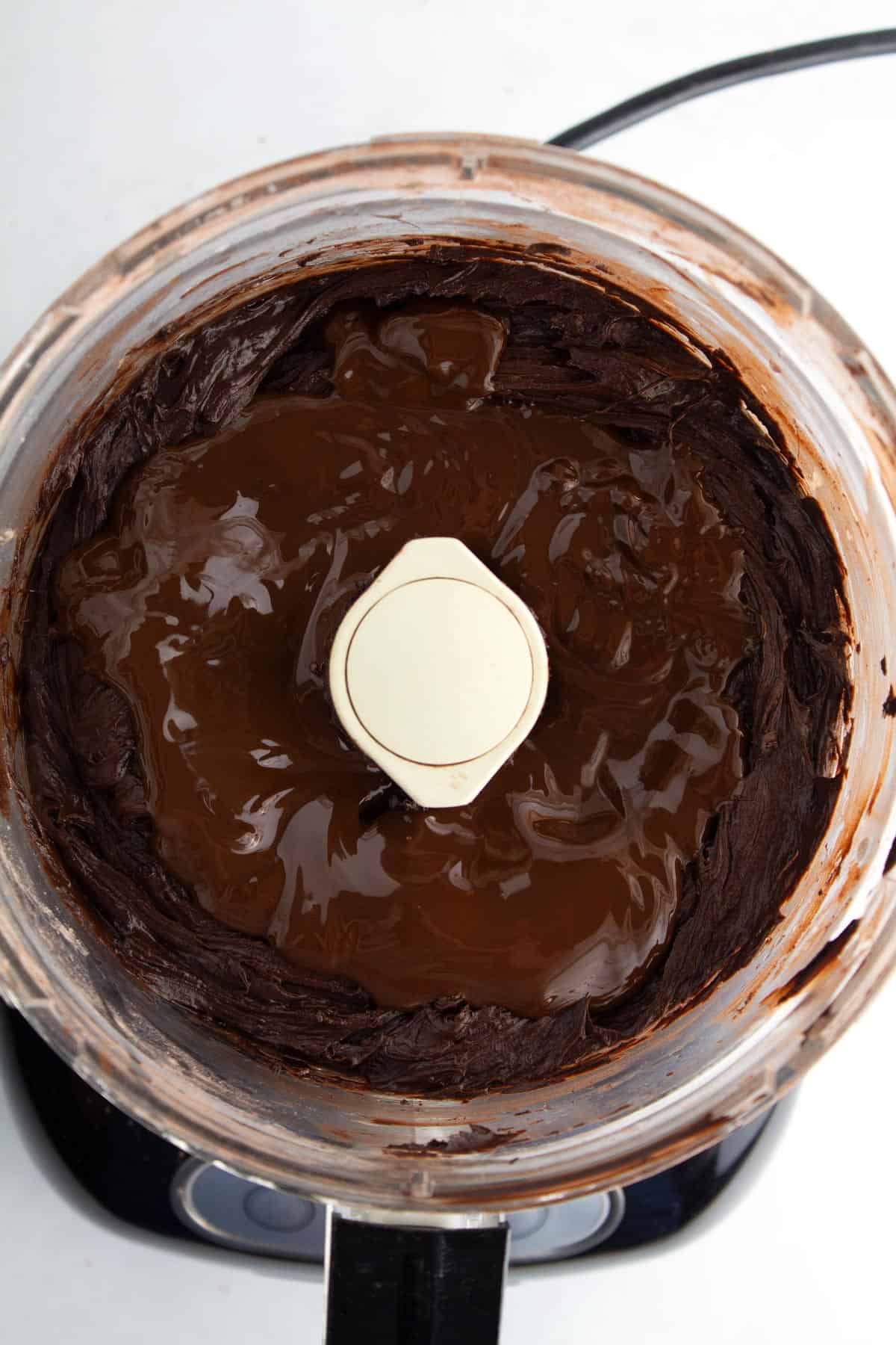 Chocolate frosting in a food processor with melted chocolate poured on top.
