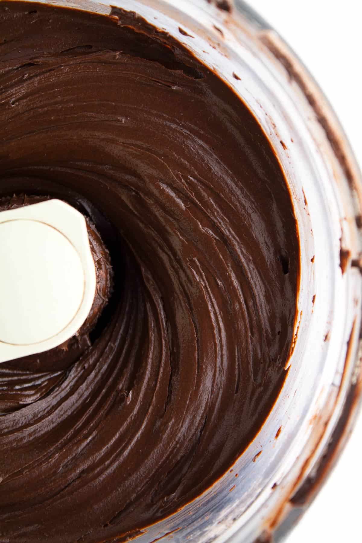 Overhead view of the right side of a food processor with chocolate fudge icing swirled inside.