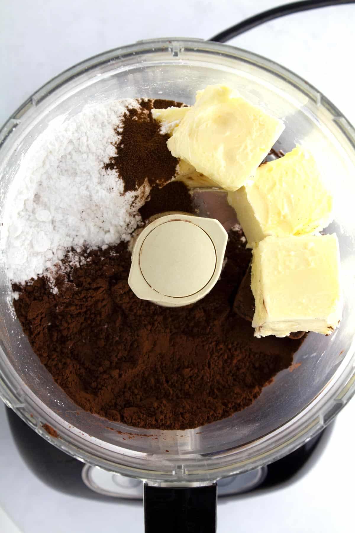 Ingredients for chocolate frosting in a clear food processor before combining.