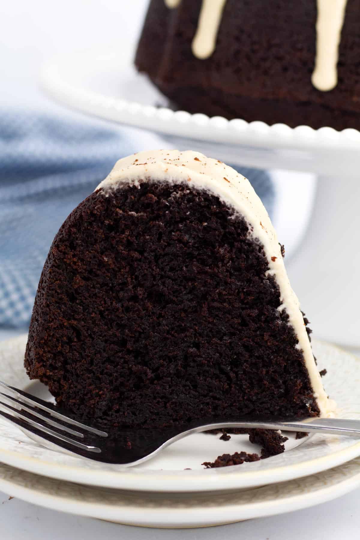 Slice of Kahlua cake on a stack of plates with a fork resting in front and the bundt cake on a cake stand in the background.