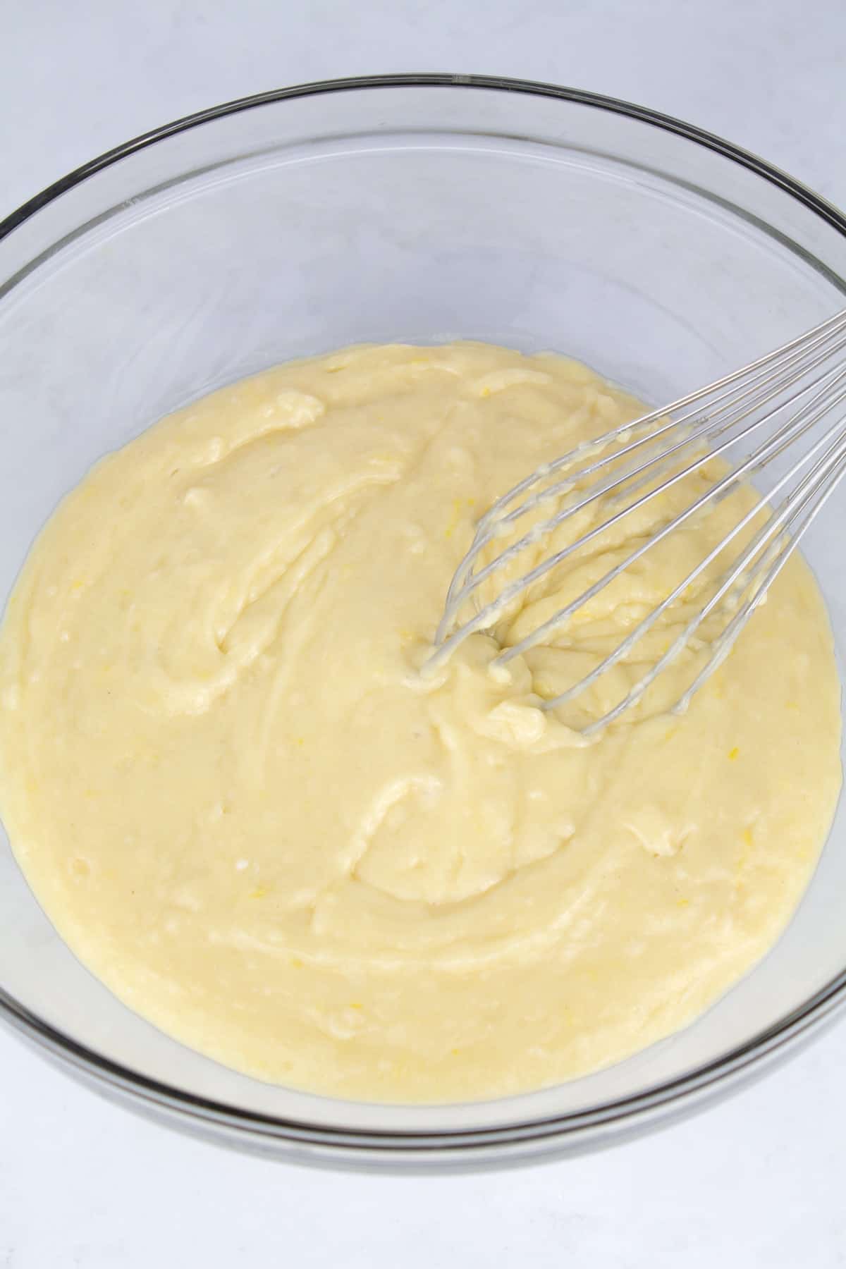 Finished cake batter in a clear glass bowl with a whisk sitting in the back of the bowl.