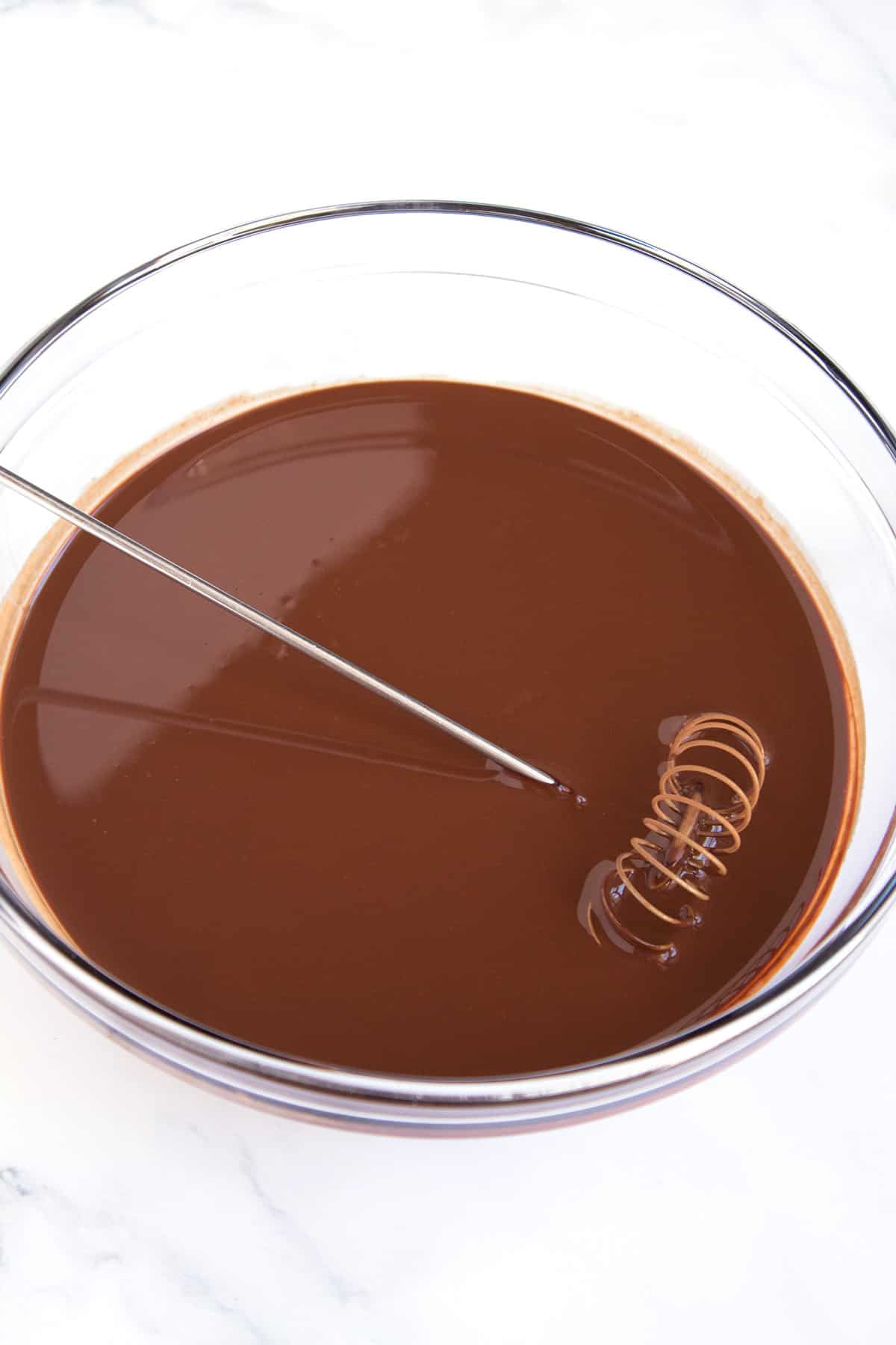 Glass bowl of hot coffee and cocoa powder combined with a whisk resting in the bowl.