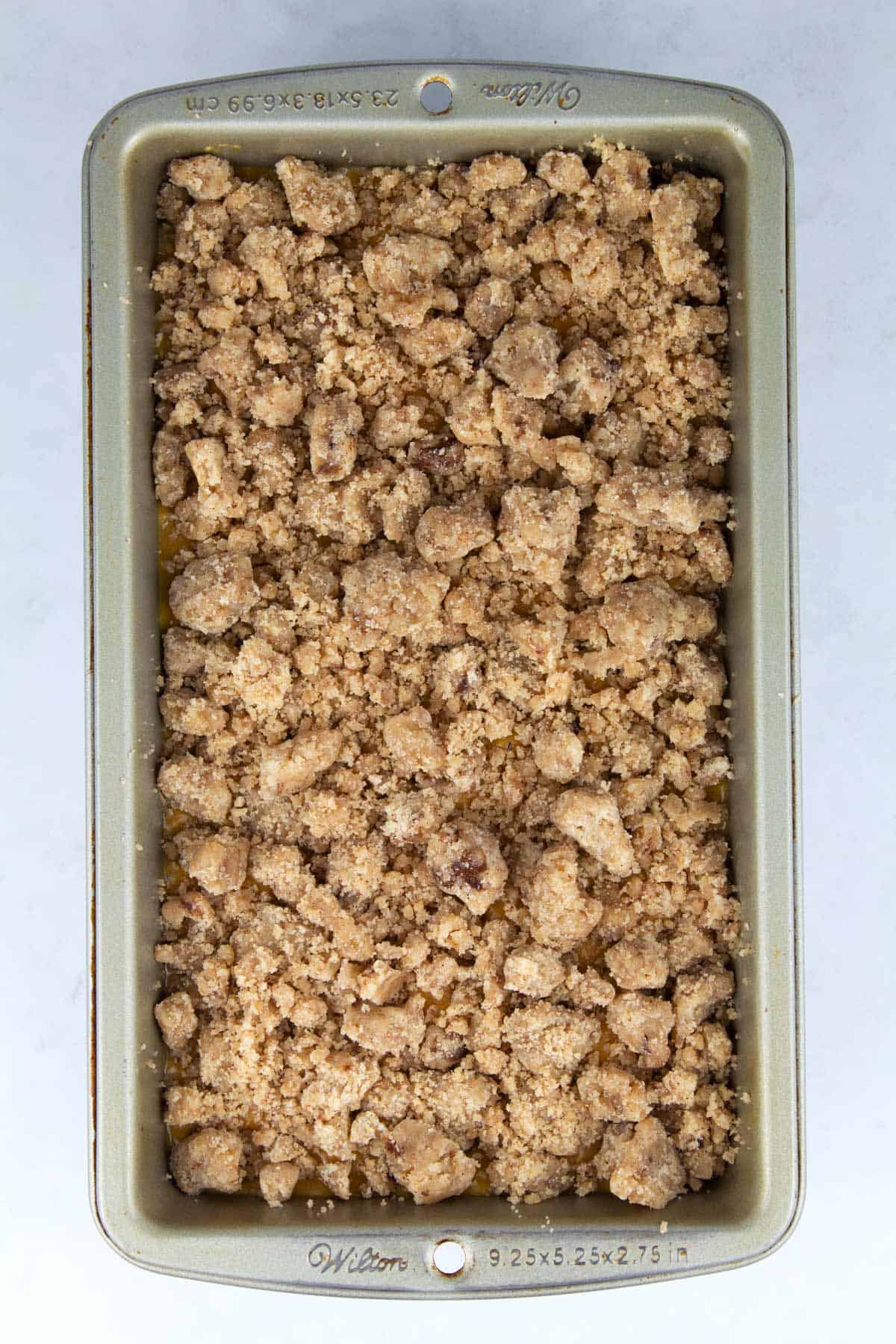 Overhead view of a loaf pan filled with pumpkin bread batter and sprinkled with crumble topping.