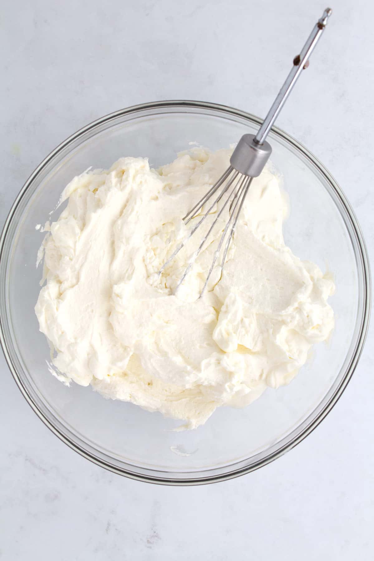 An overhead view of mascarpone whipped cream in a clear glass bowl with a whisk.