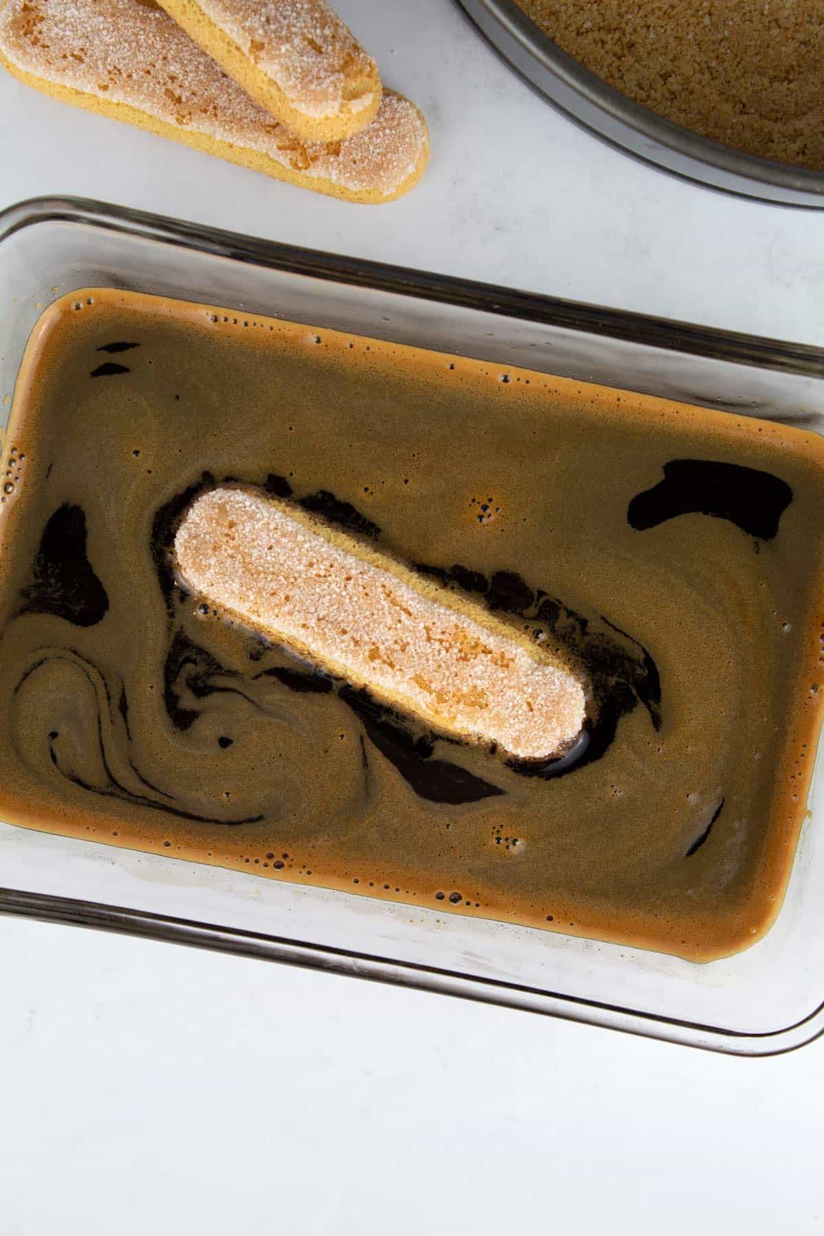An overhead view of a ladyfinger being soaked in an espresso Kahlua mixture.