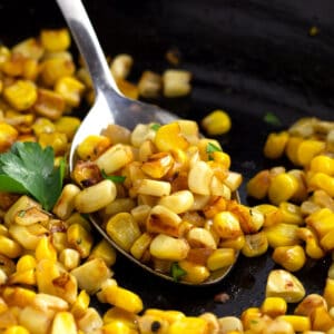 Serving spoon full of caramelized pieces of roasted corn.