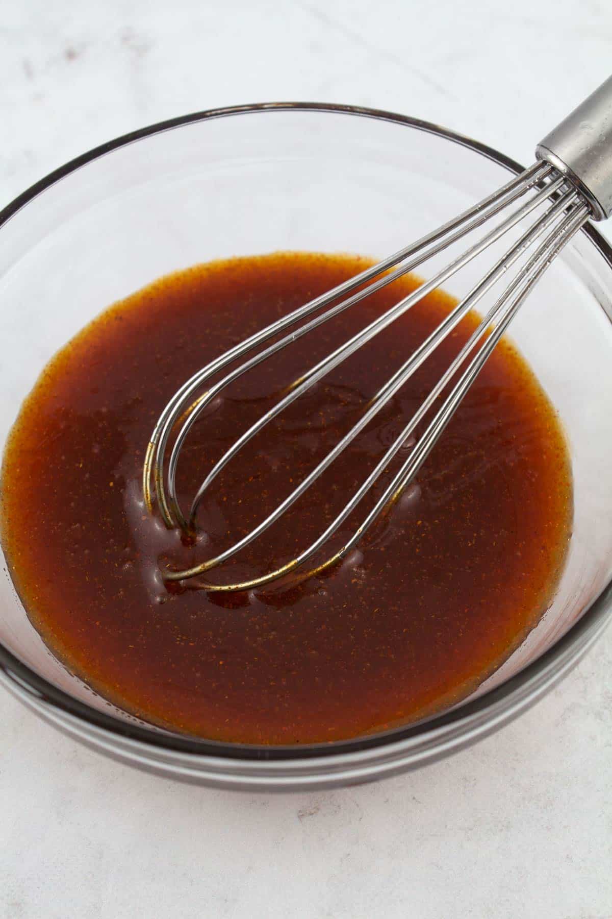 Hot honey sauce mixed in a glass bowl with a whisk.