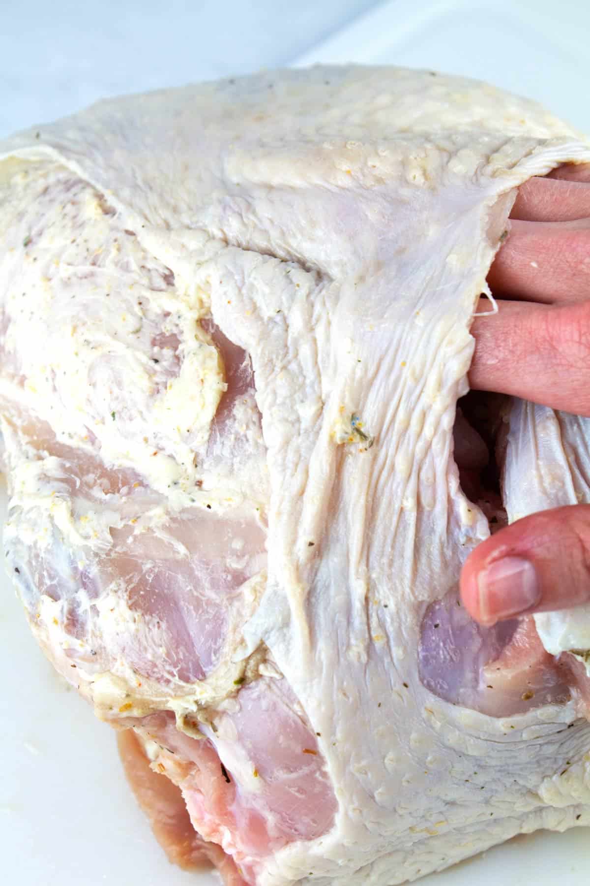 Hand rubbing flavored butter under the skin of the turkey breast.