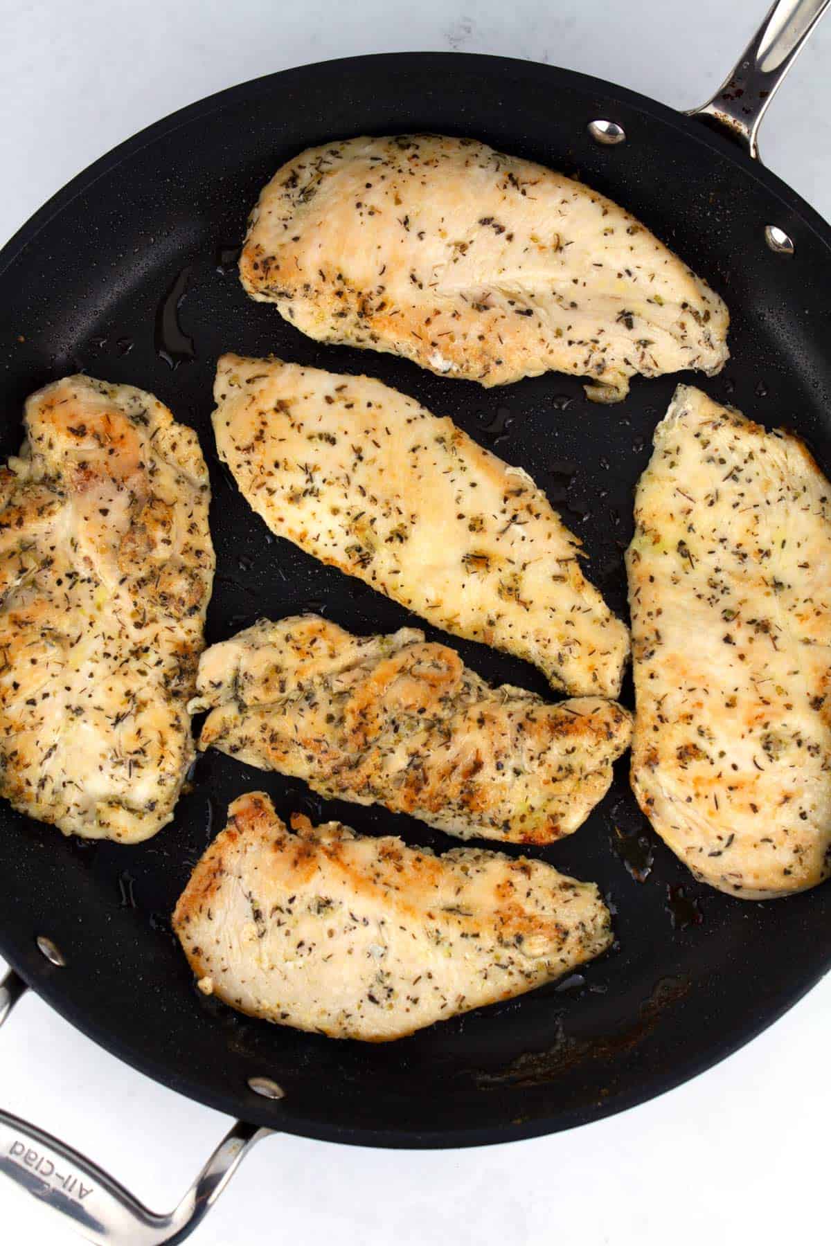 Six pieces of chicken seared in a black skillet.
