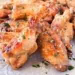 Two crispy garlic parmesan wings balancing on small pile of baked chicken wings.