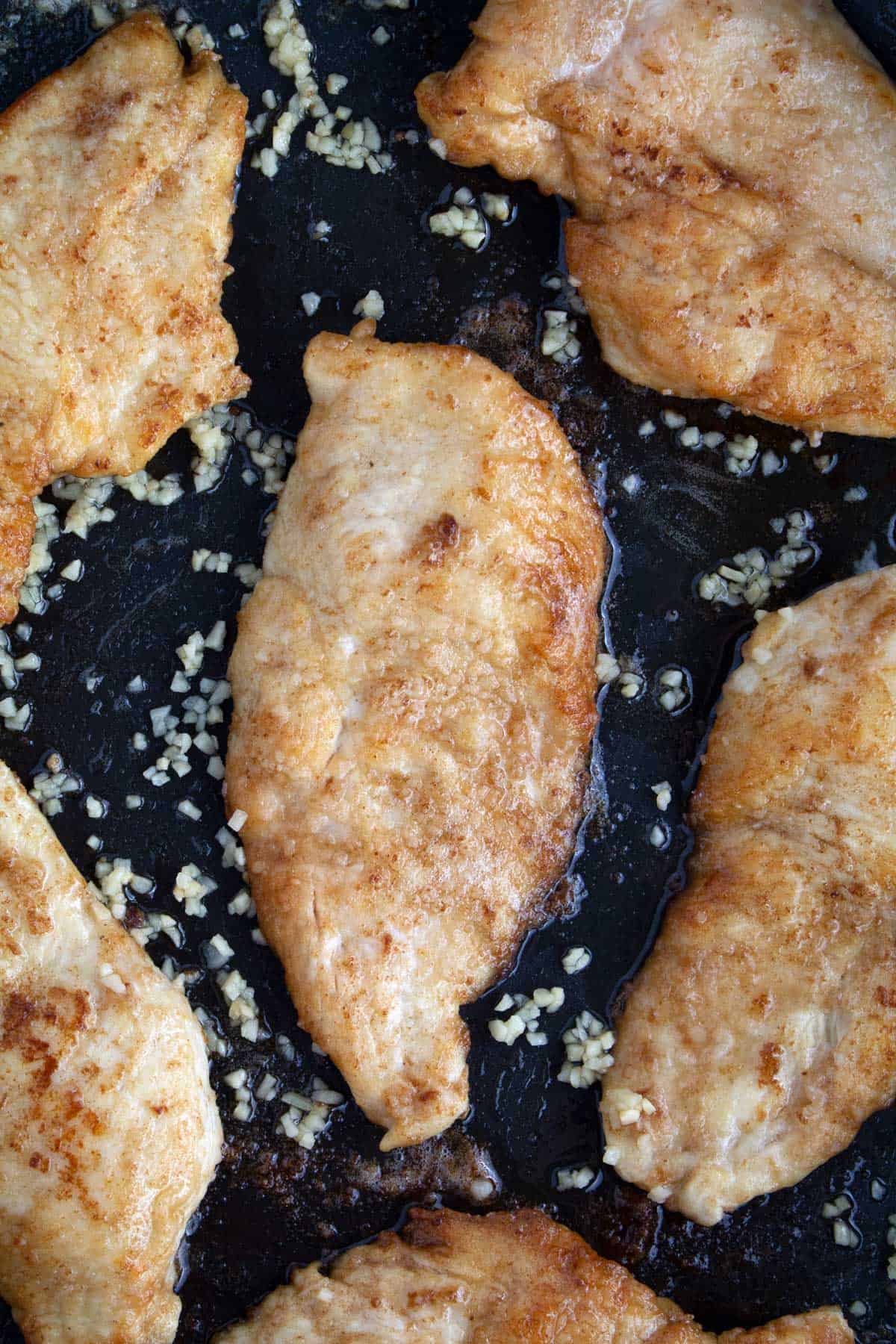 Overhead of chicken cooked in a non-stick skillet with minced garlic added to the pan.
