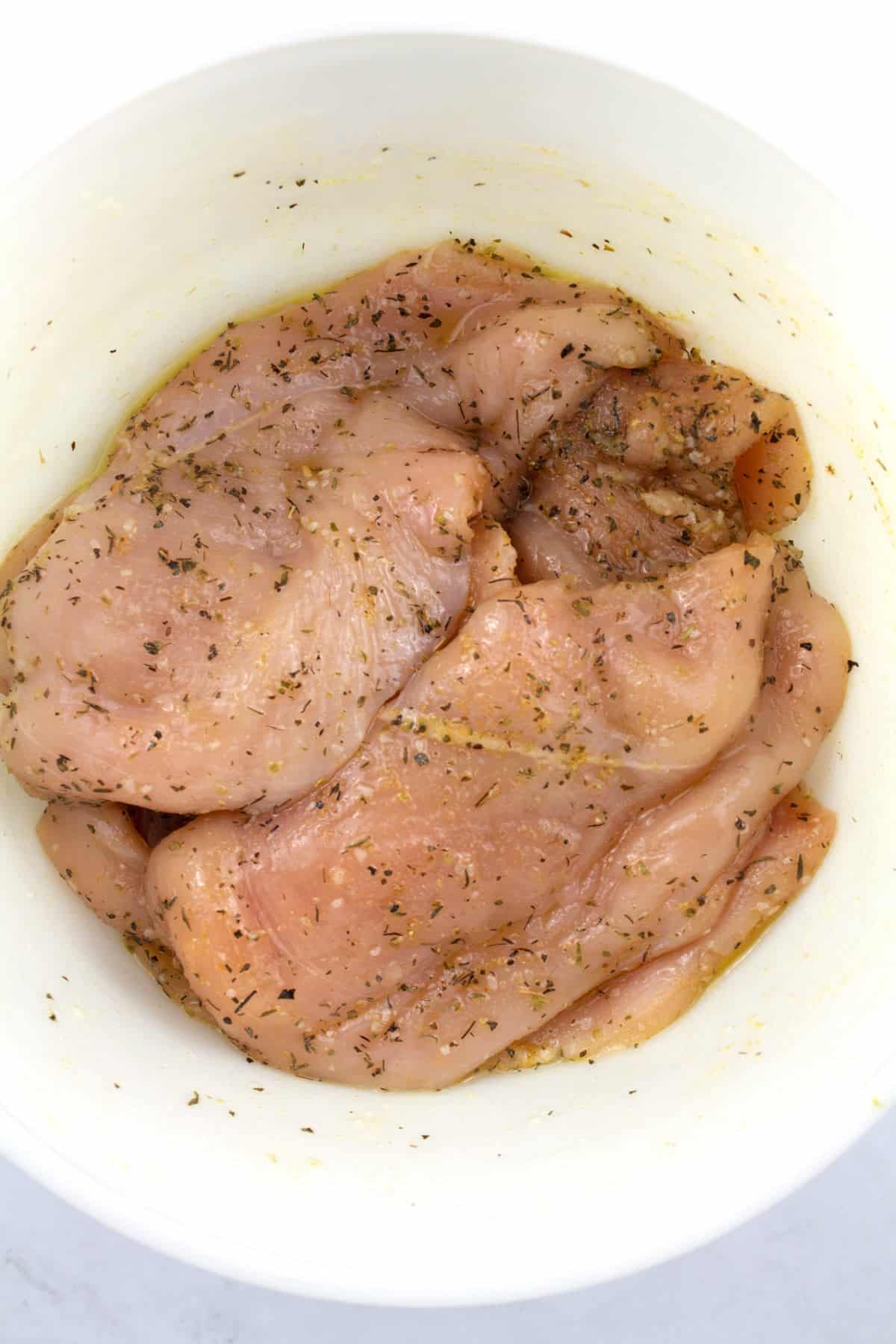 Raw chicken breasts seasoned in a white bowl.