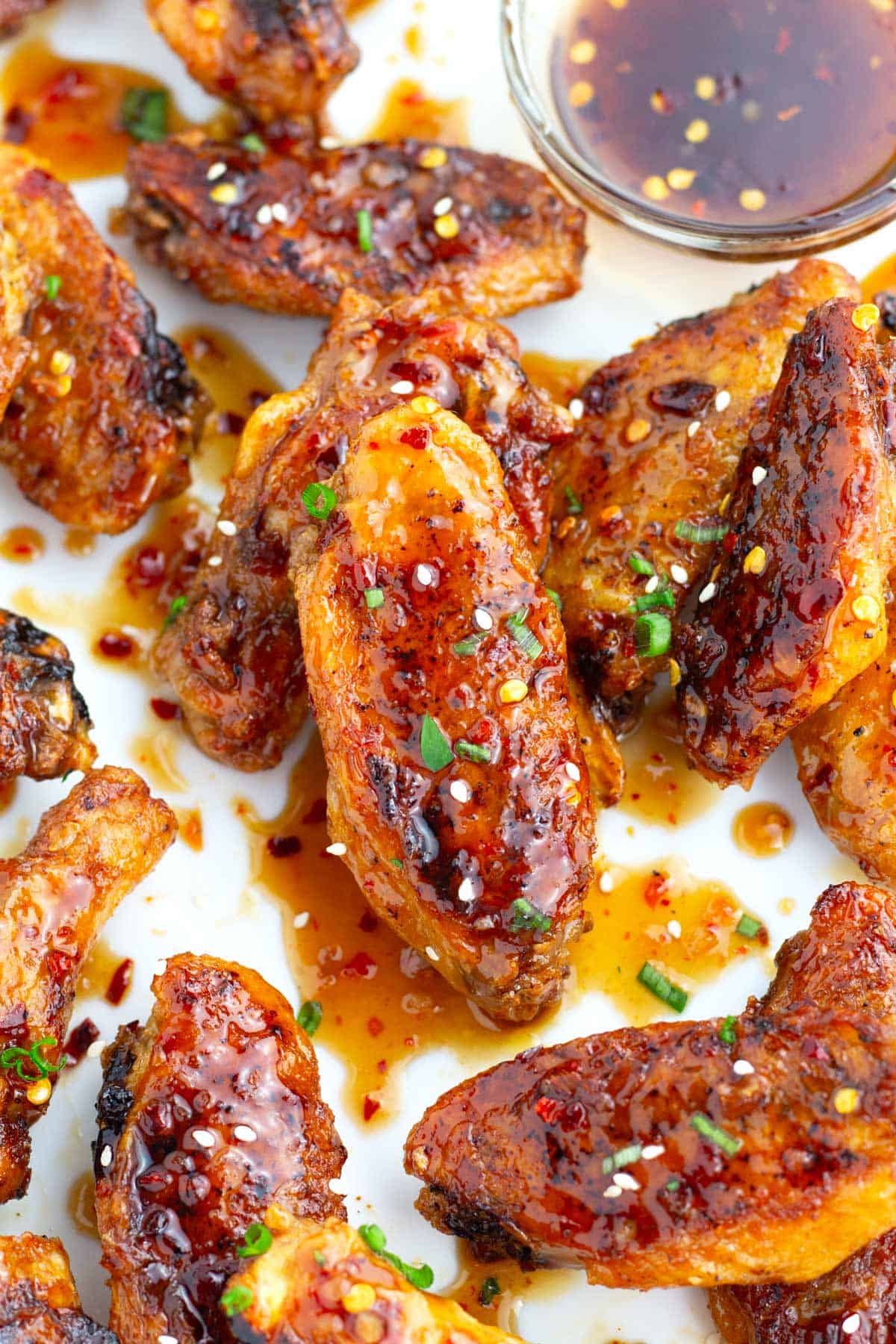Pile of sweet and savory wings on a platter sprinkled with sesame seeds and green onions.