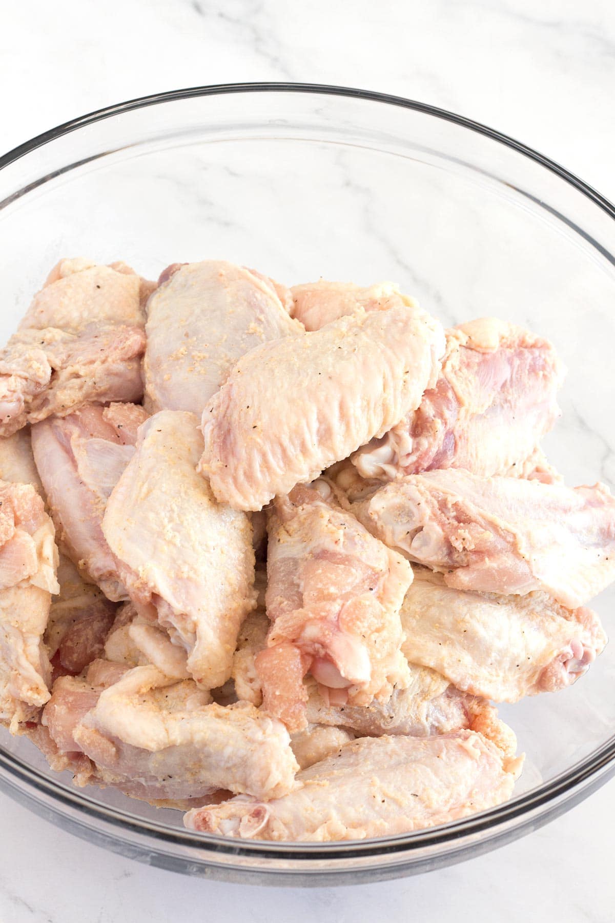 Chicken wings in a bowl tossed with baking powder and seasoning.