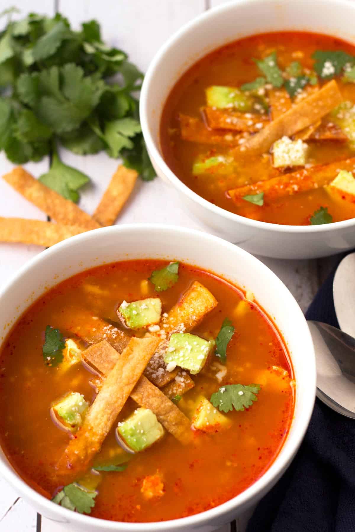 Mexican Tortilla Soup topped with creamy avocado, crispy tortilla strips, cotija cheese, lime juice, and fresh cilantro.